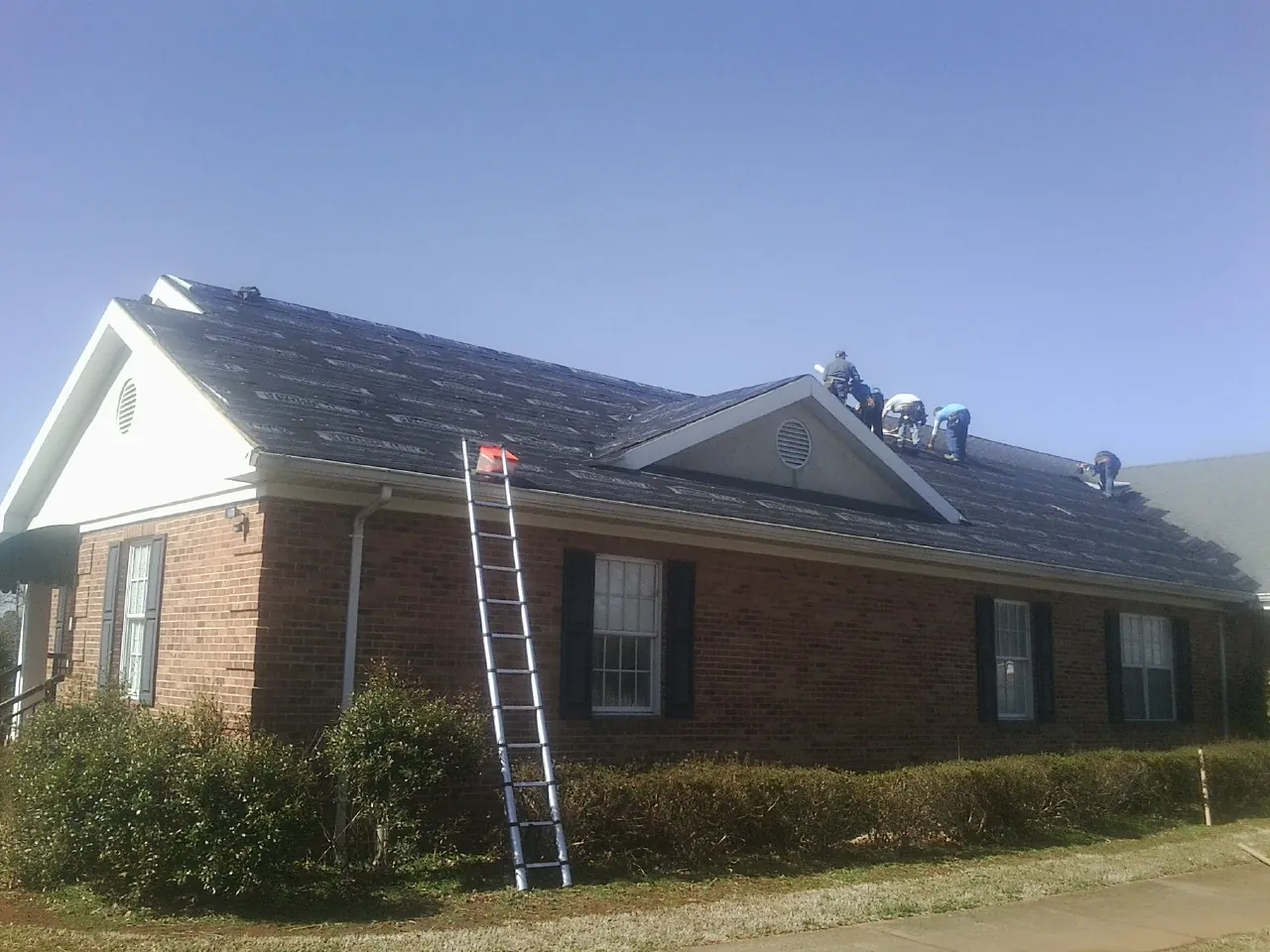 Crew tearing shingles off a brick ranch roof with a ladder set — Metal Roof Repair work by our crew in East Berlin