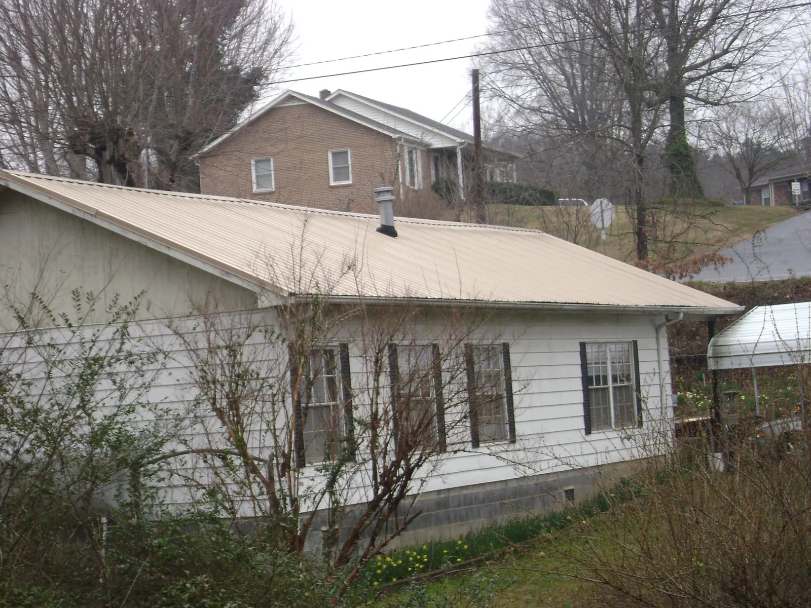 Tan metal roof on a white sided house set into a hillside — Commercial Roofing by Roofing Brothers in East Berlin